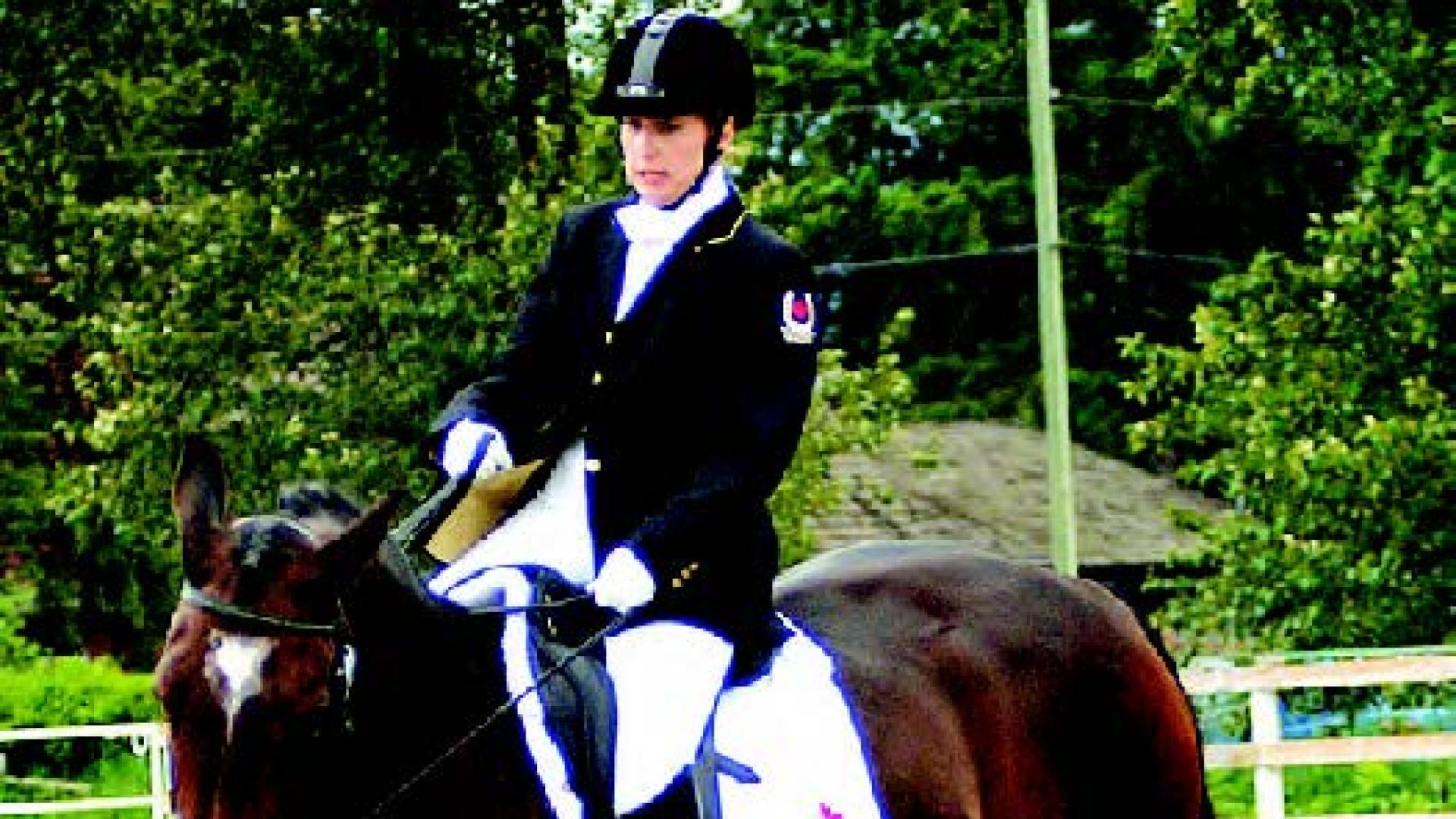 Jennifer McKenzie rides a chestnut-brown horse in an arena.